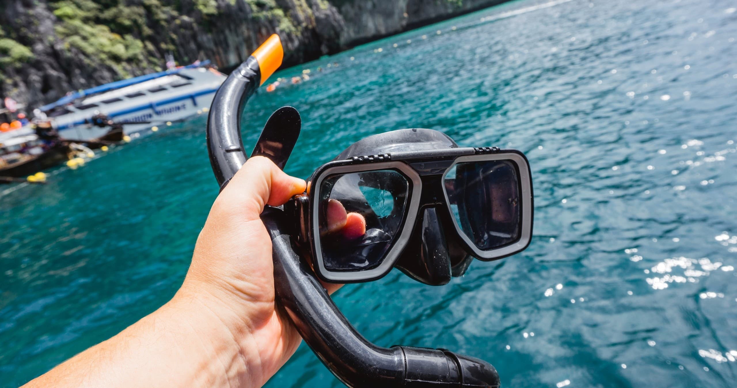 Hand holding snorkel mask over turquoise sea before snorkeling