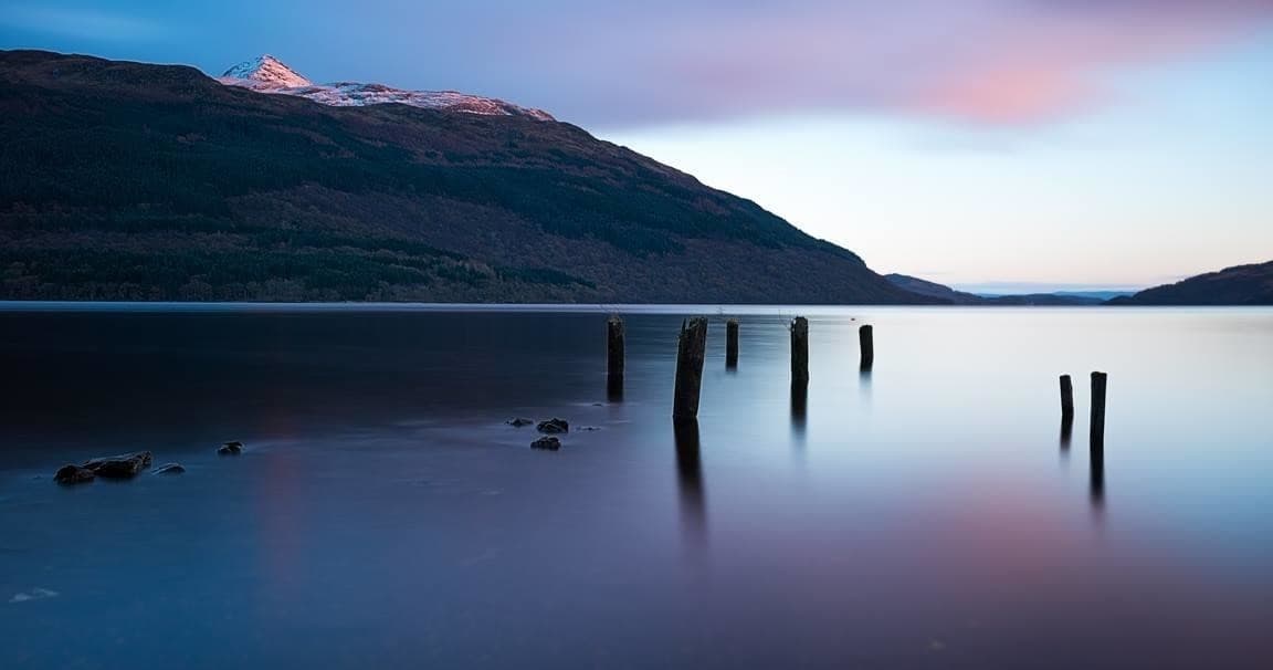 Morning loch with wooden posts, calm waters for landscape photography