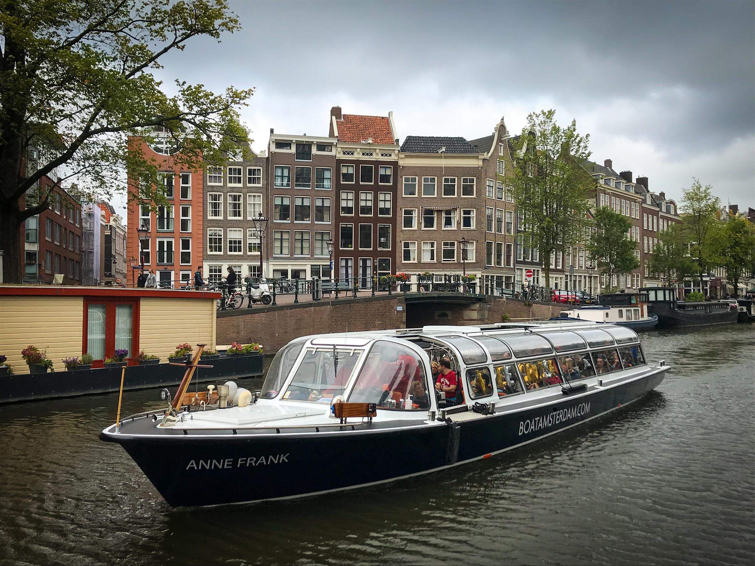 Glass-roofed canal tour boat cruising past Amsterdam canal houses