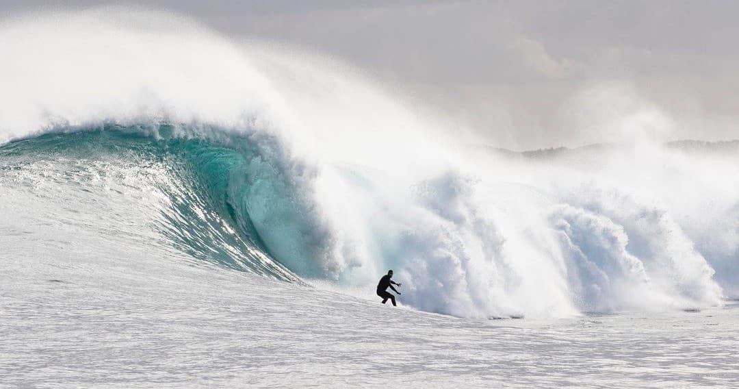 Surfer riding a massive ocean wave in dramatic coastal surf