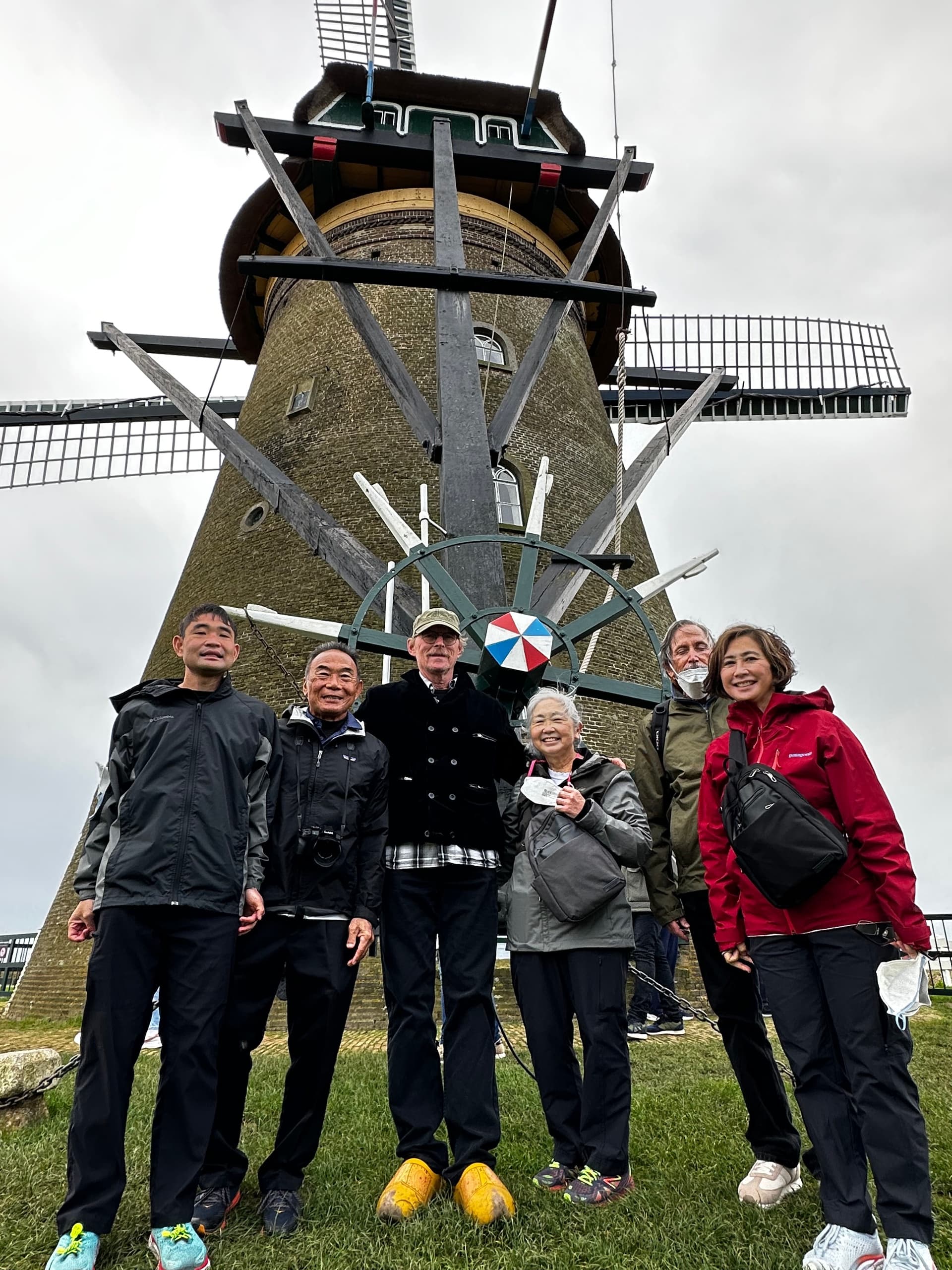 Group posing by traditional Dutch windmill on grassy hill during tour