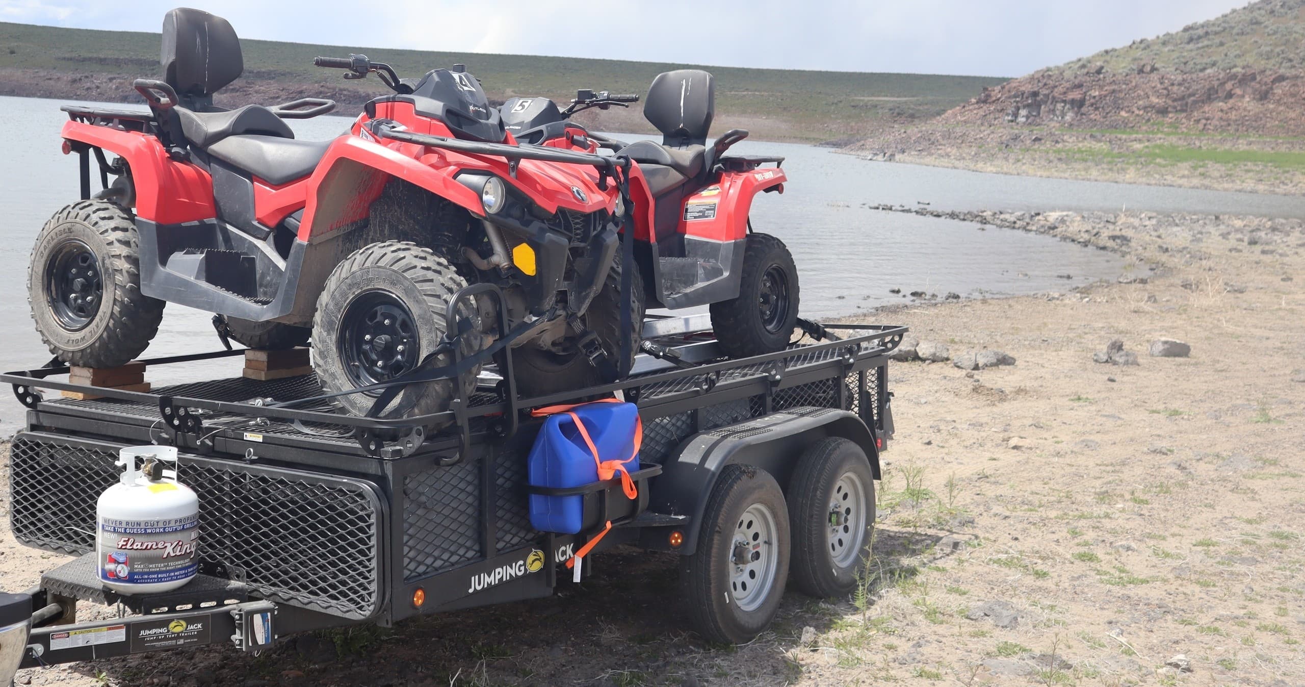 Two ATVs loaded on a trailer by a lakeshore for off-road touring