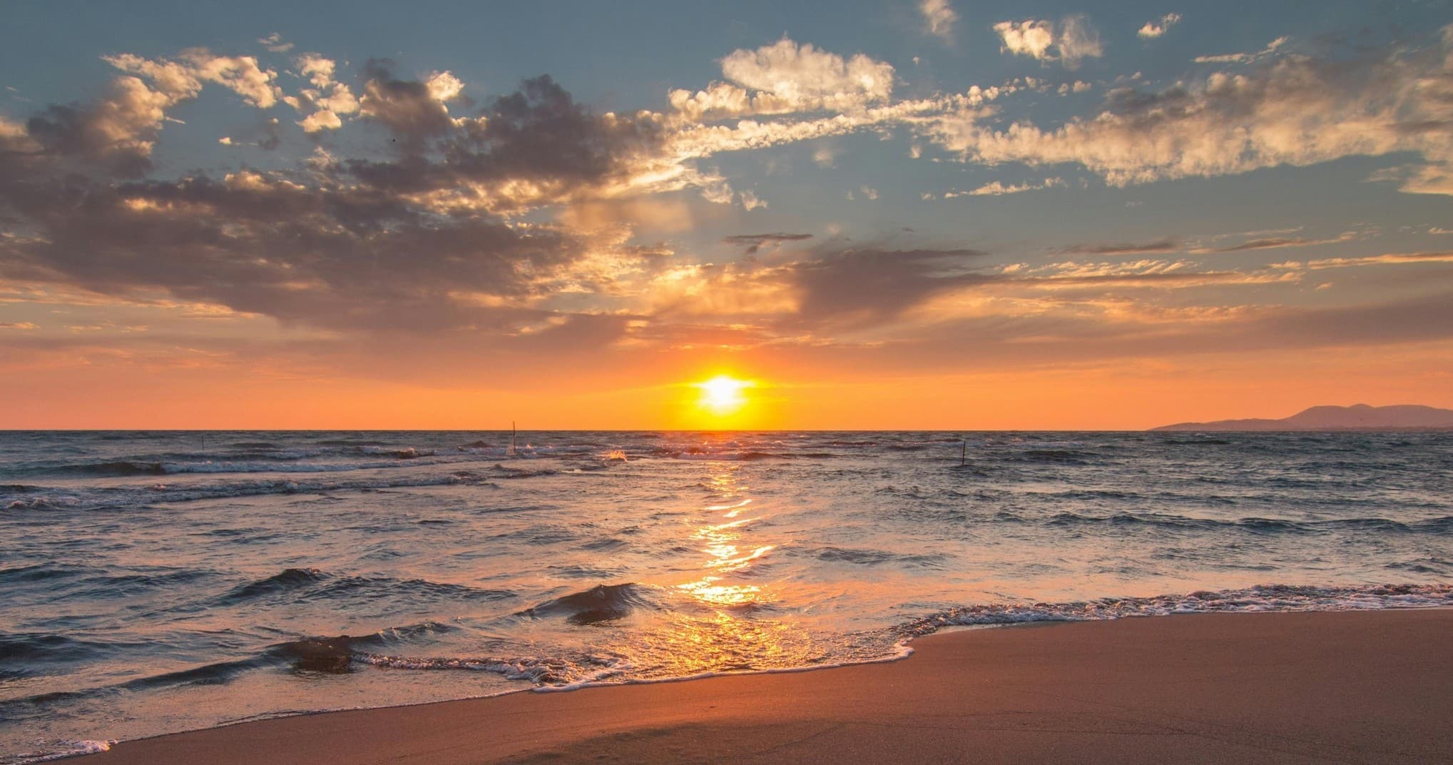 Sunset over sandy beach with calm ocean waves and horizon
