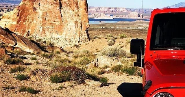 Red Jeep at desert trailhead beside sandstone formations and open plain