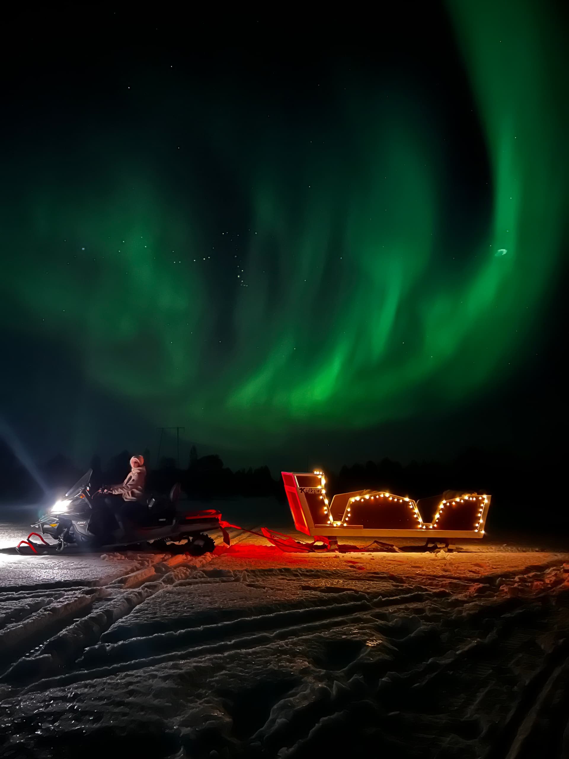 Northern lights above sled and illuminated snow camp at night
