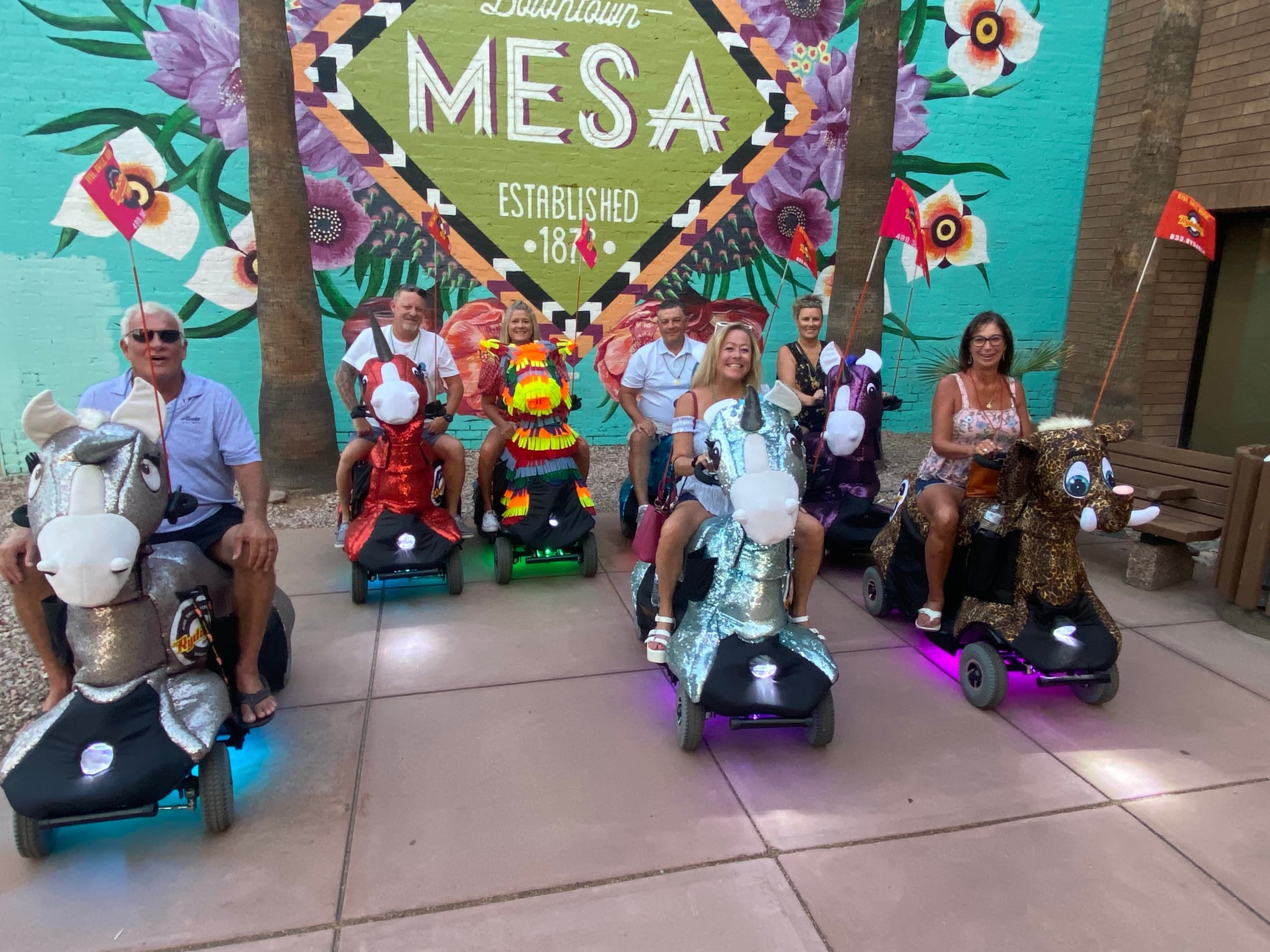 Riders on painted scooter animals in front of Mesa mural wall