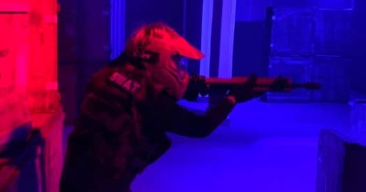 Player aiming rifle in neon-lit indoor CQB course during skirmish