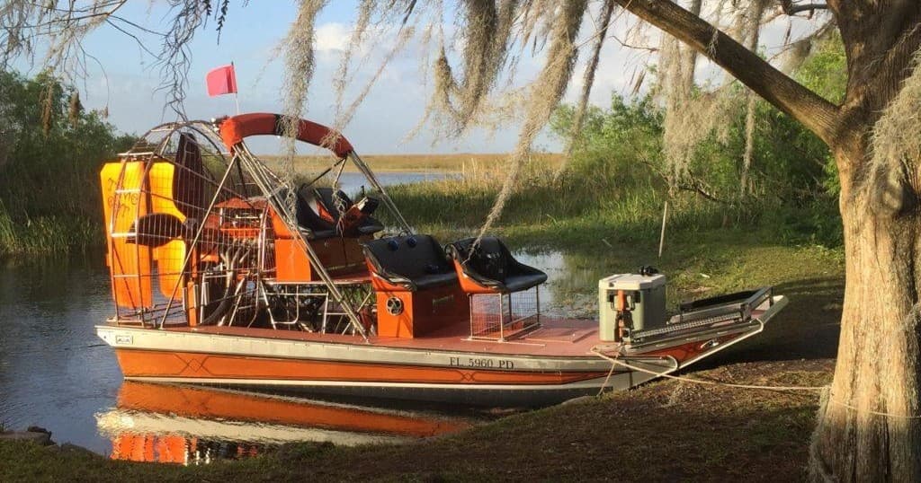 Orange airboat moored on a scenic Florida marsh shoreline at sunset