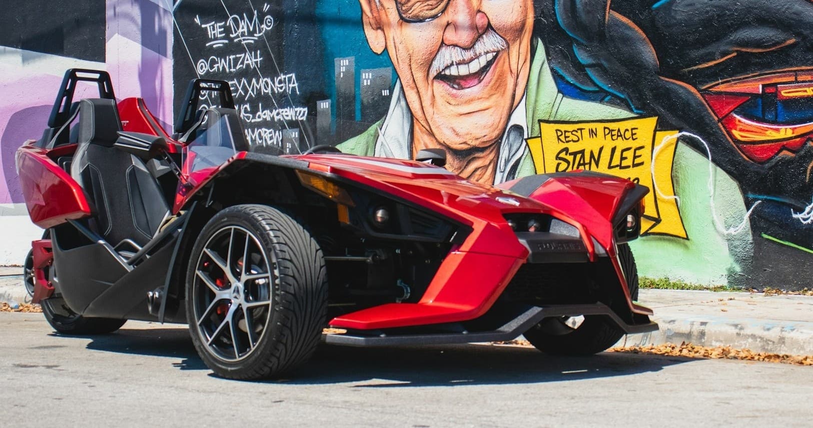 Red Slingshot parked by colorful mural, urban street rental photo