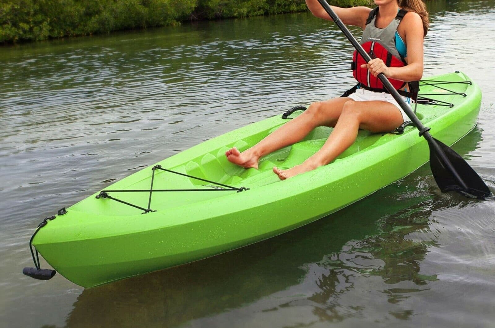Person kayaking in bright green kayak on calm lake near marina
