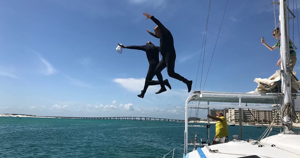 People jumping off sailboat into clear ocean during adventure cruise