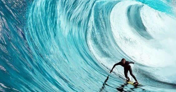 Surfer riding a giant turquoise barrel wave off ocean coast