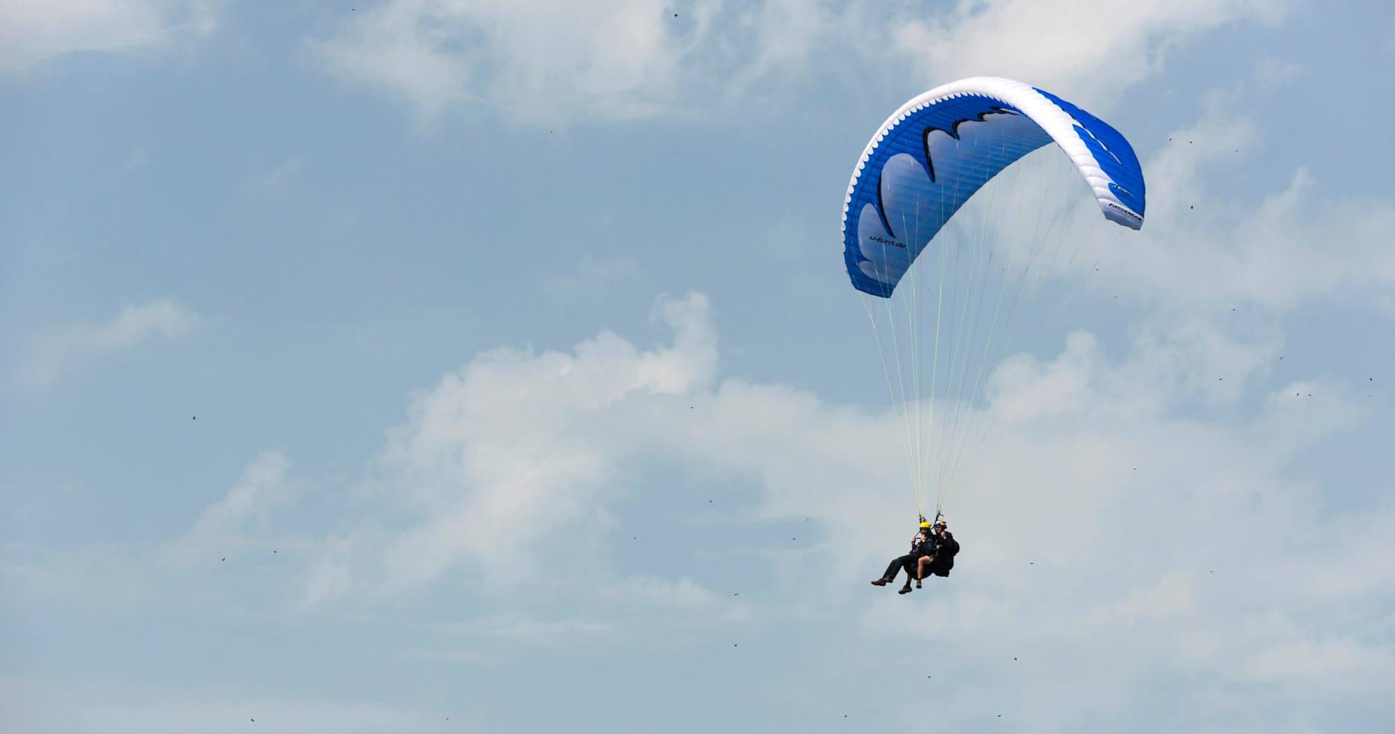Single paraglider floating in blue sky over open alpine ridge
