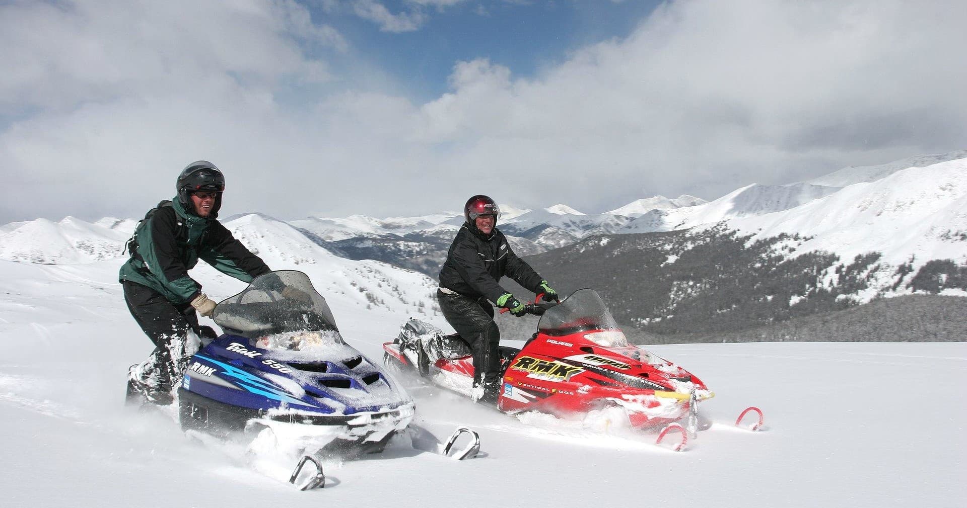 Two snowmobilers riding across snowy alpine basin with mountains