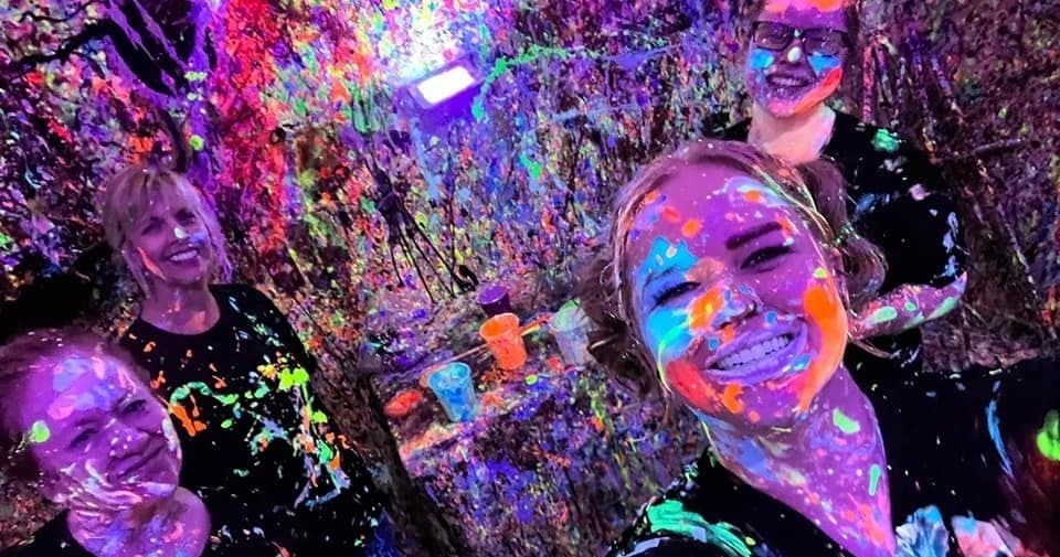 Group selfie covered in neon paint under blacklight in indoor party room