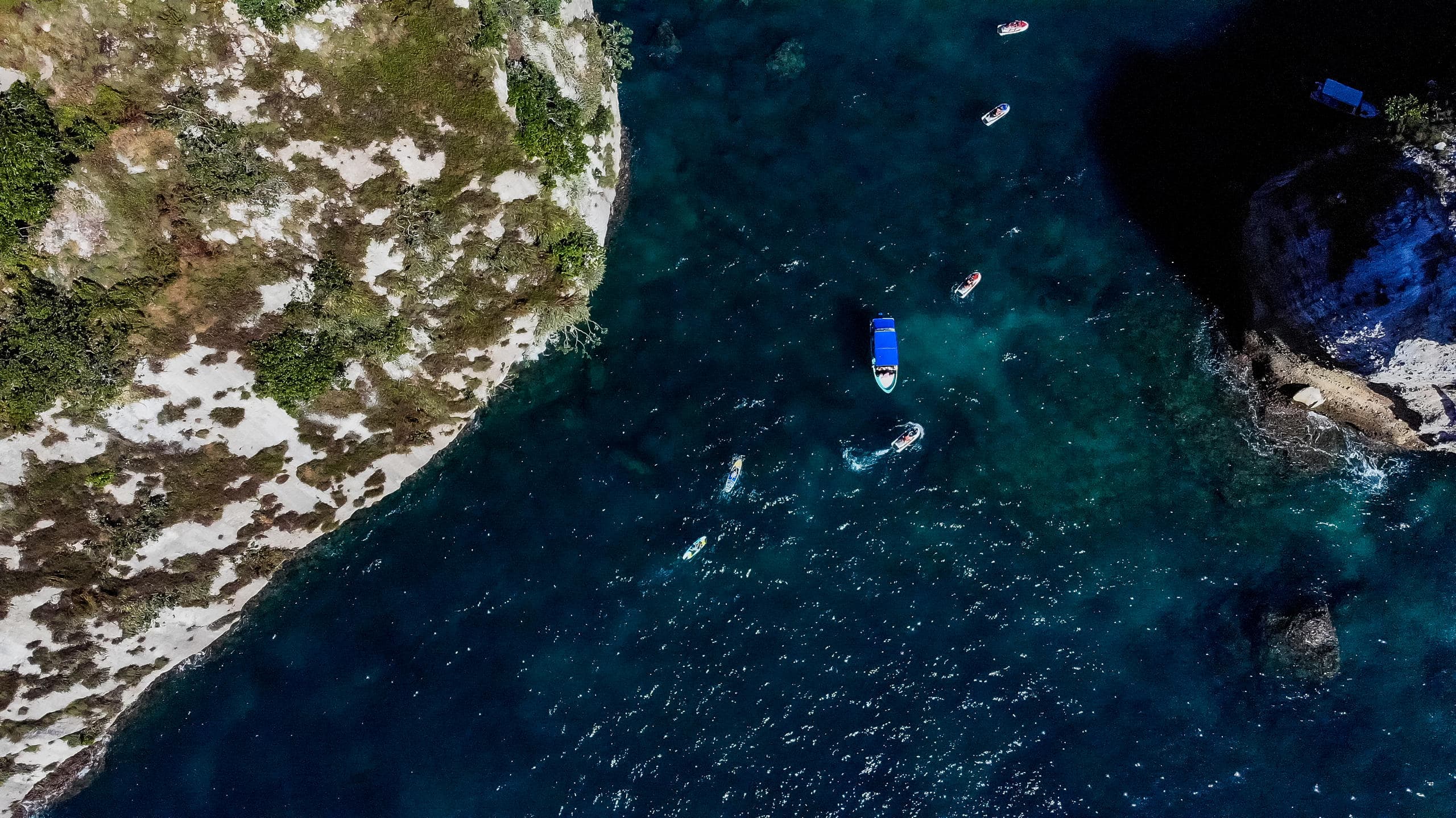 Aerial boat navigating rocky coastal cove with turquoise sea