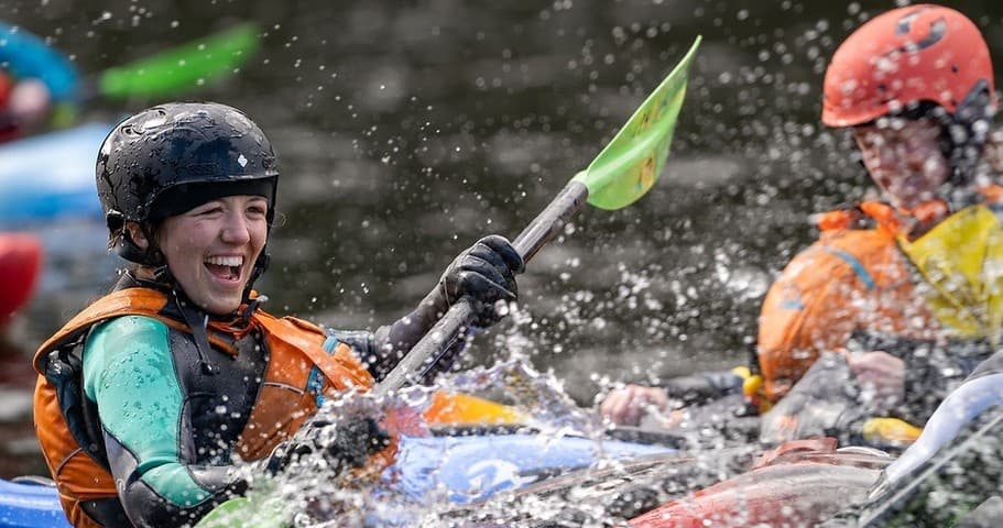 Smiling kayaker paddling through splashing whitewater rapids