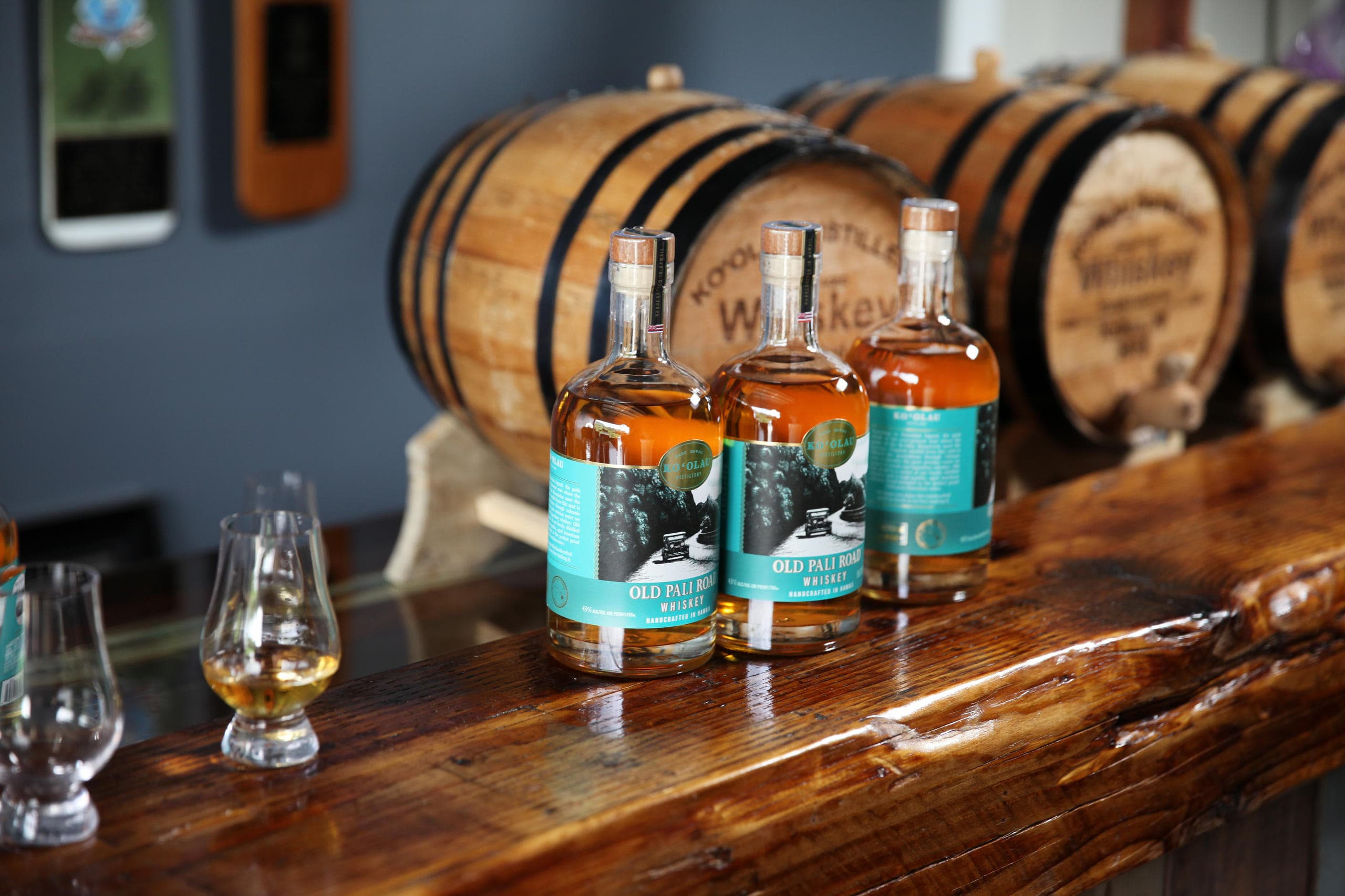 Whiskey bottles and glasses on bar with oak barrels behind