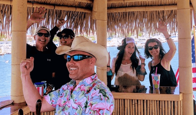 Passengers cheering aboard small tiki boat near marina during day cruise