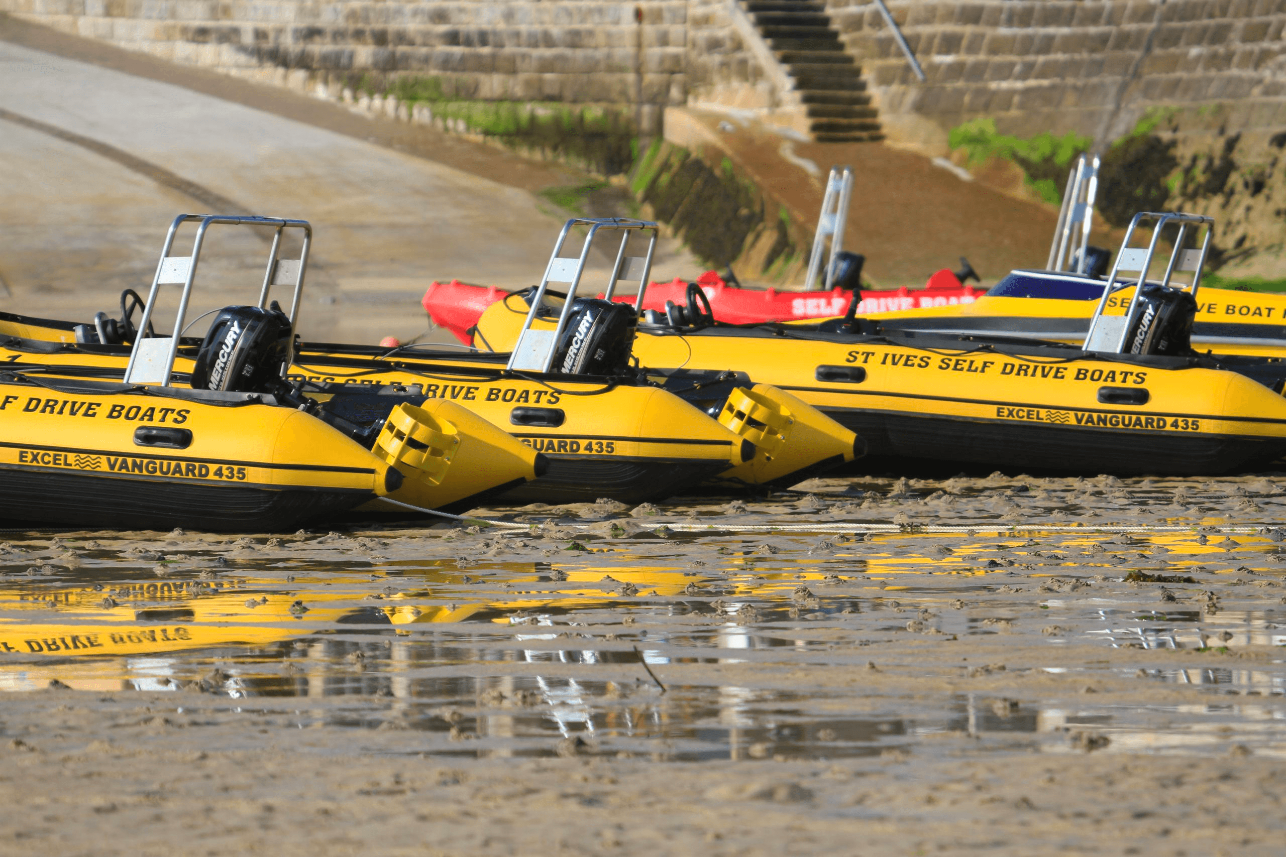 Yellow self-drive boats lined along tidal beach at low tide