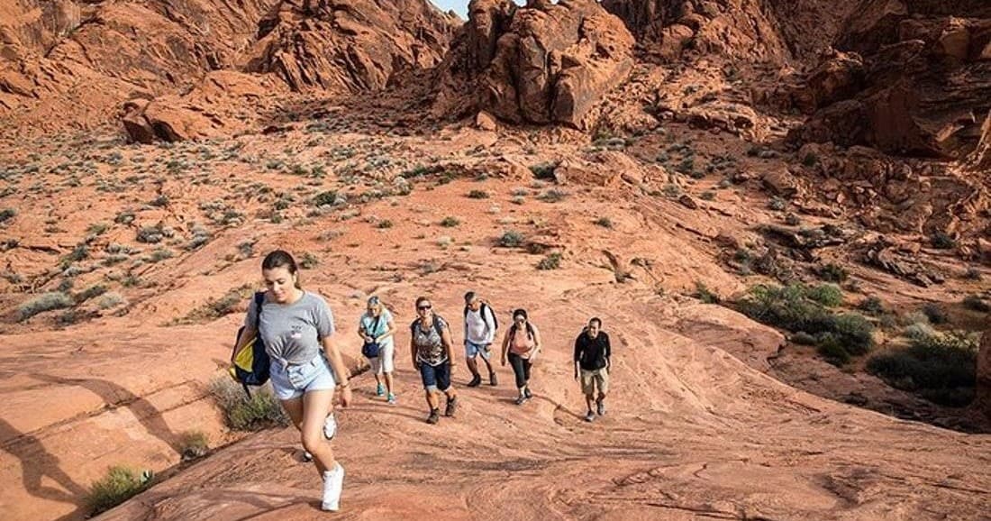 Group hiking across red rock slopes in arid desert canyon