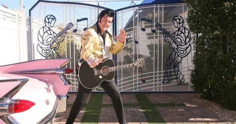 Elvis impersonator performing outdoors by vintage car at chapel gate