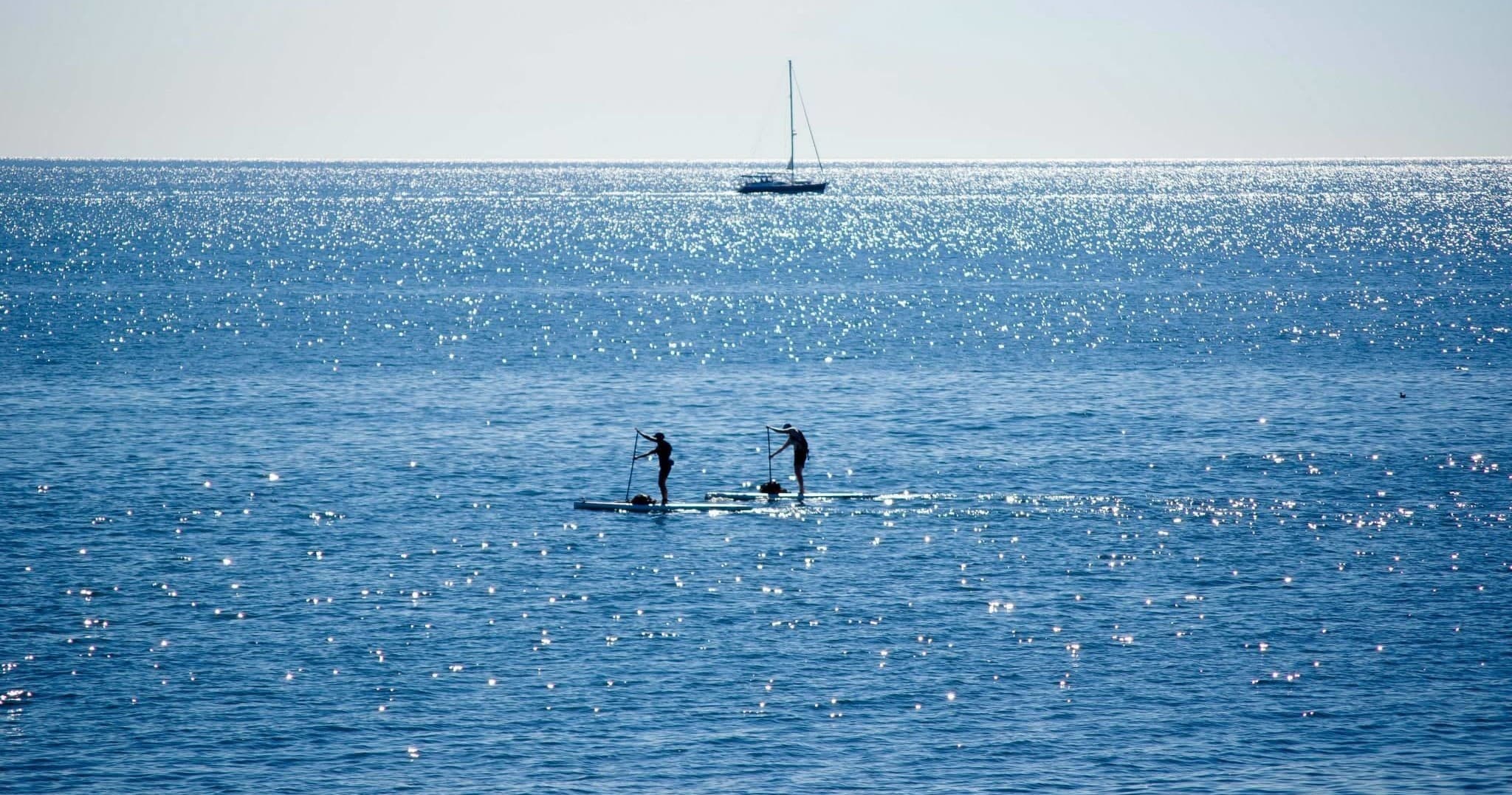 Kayakers paddling on open ocean near a distant sailboat