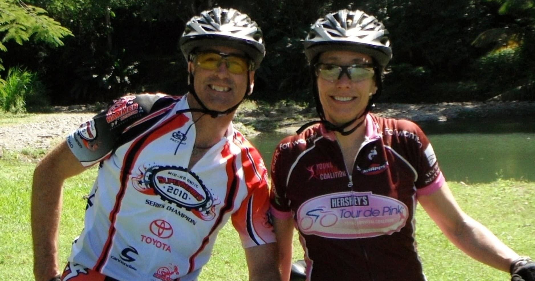 Two cyclists smiling by pond during recreational trail ride