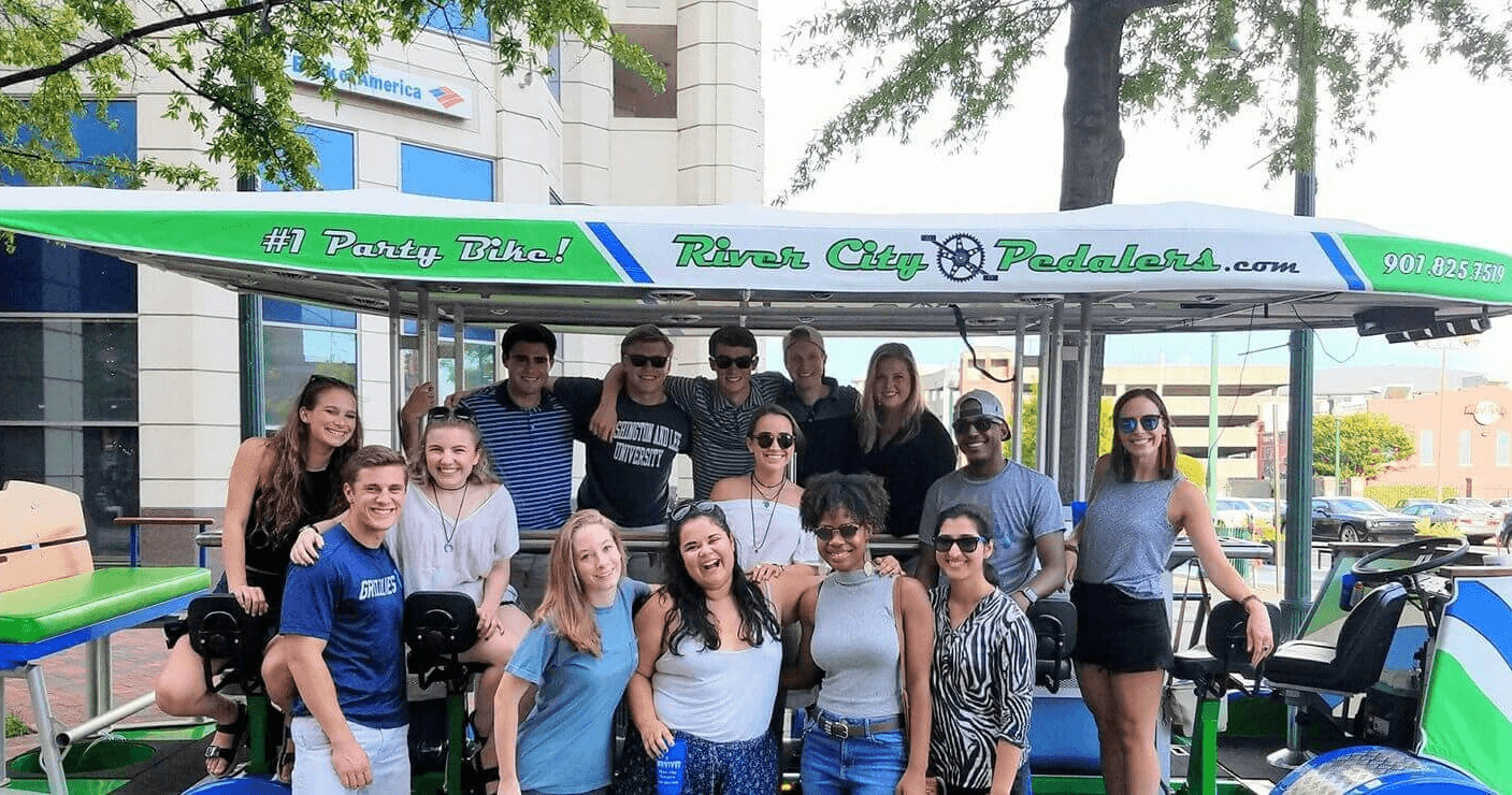 Large group on pedal bar tour along tree-lined downtown street