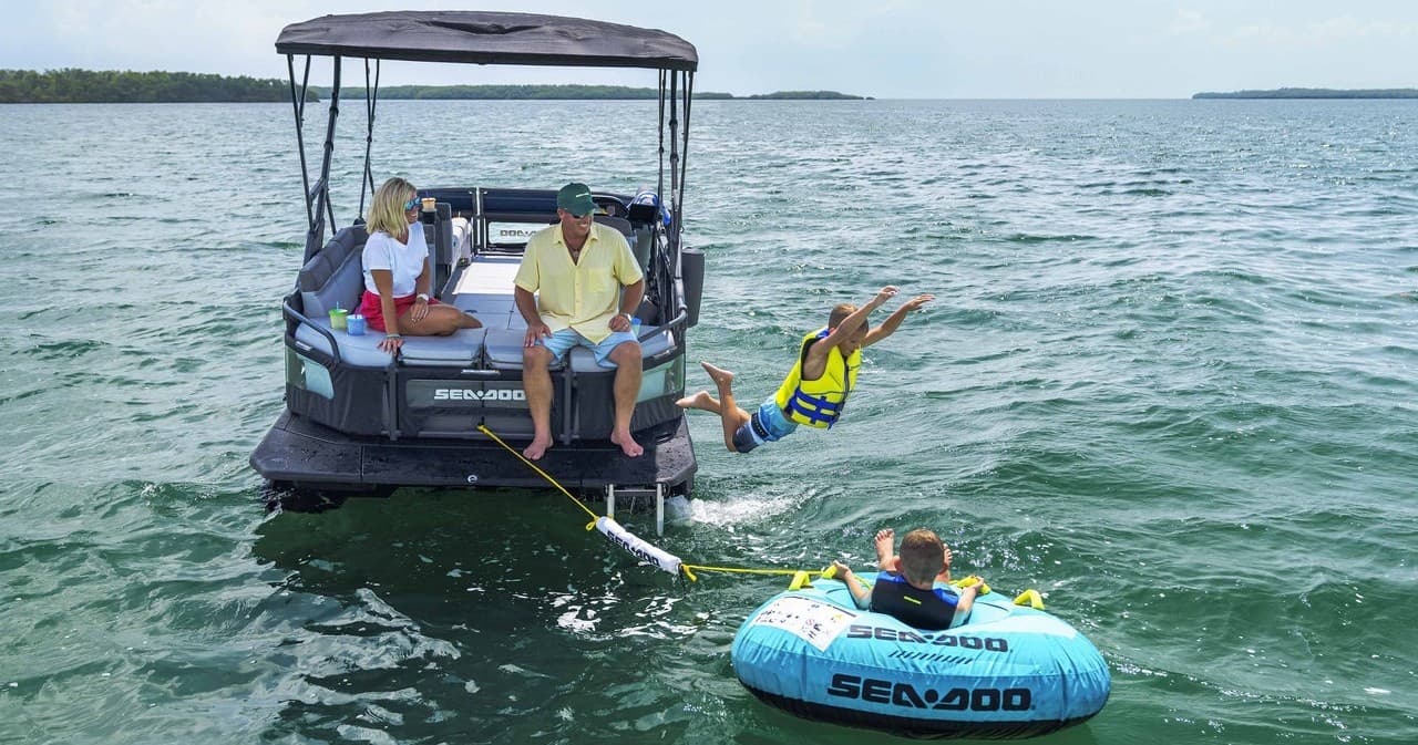 Family tubing behind pontoon boat on open lake