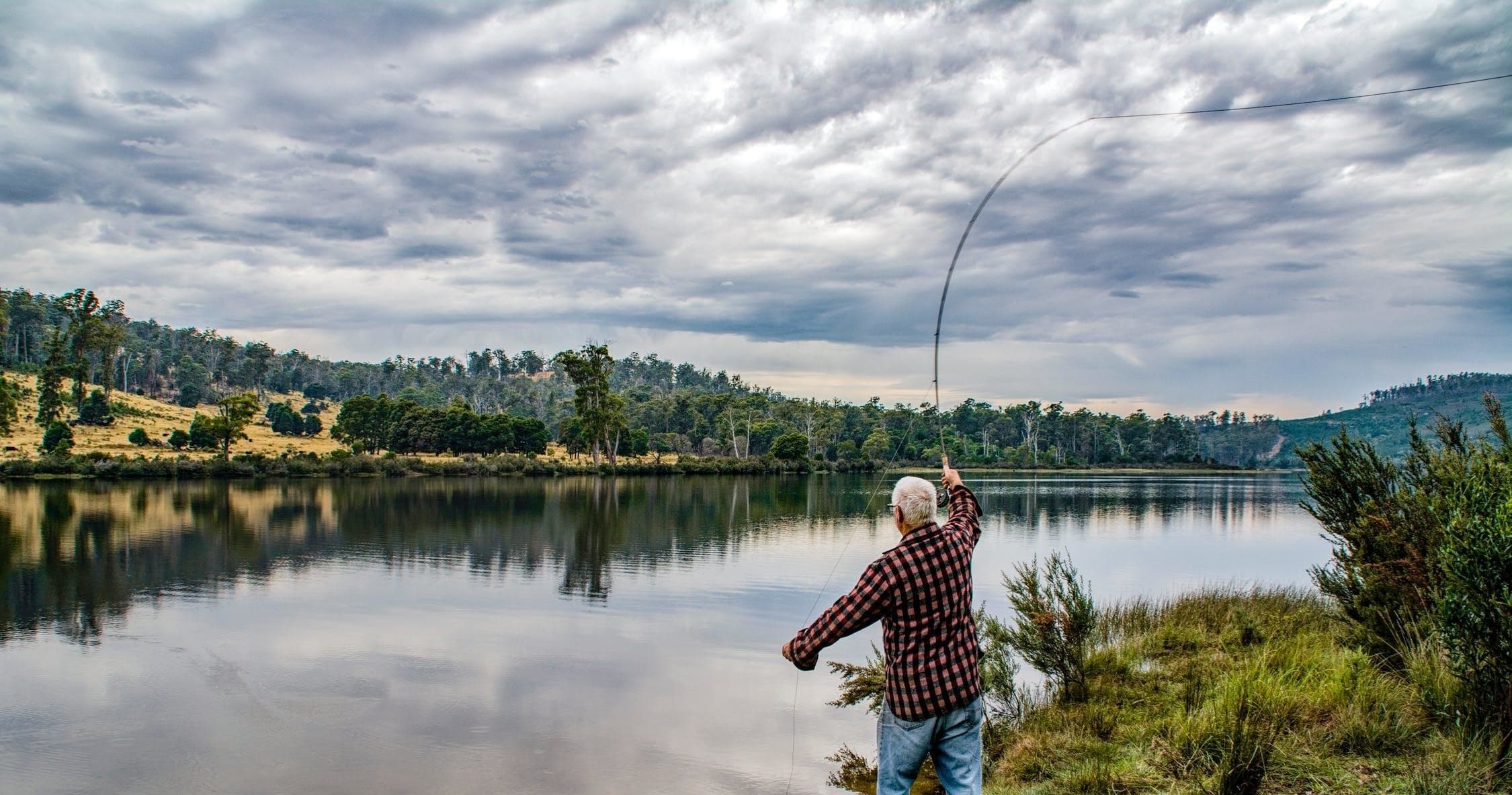 Angler casting on calm mountain lake at wooded shoreline