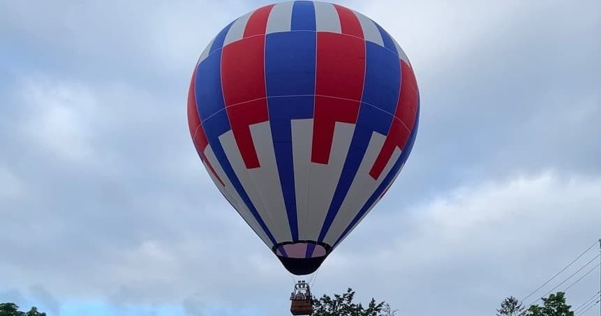 Close-up hot air balloon ascending against cloudy sky overhead