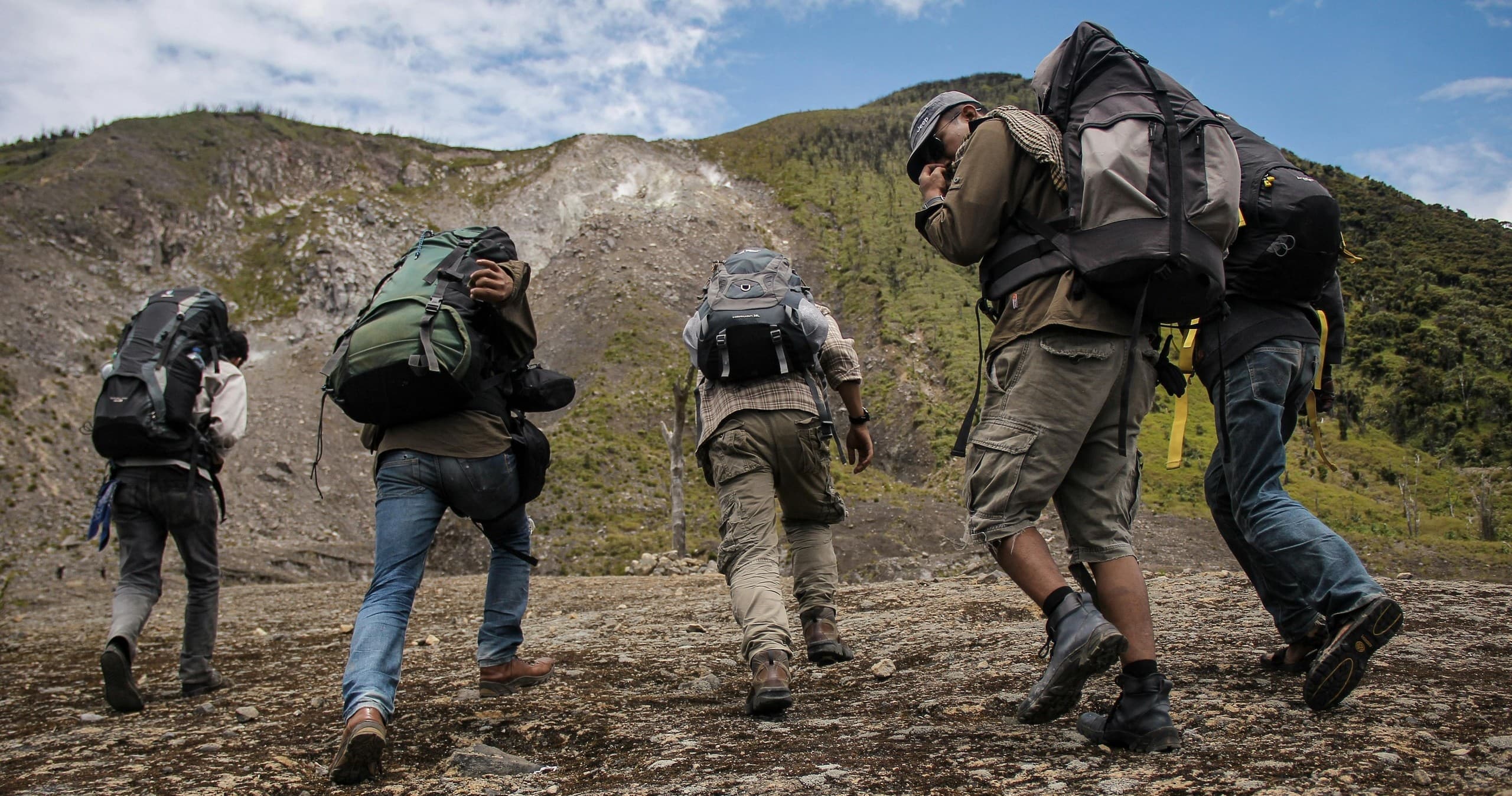 Backpackers trekking over rugged mountain trail under blue sky