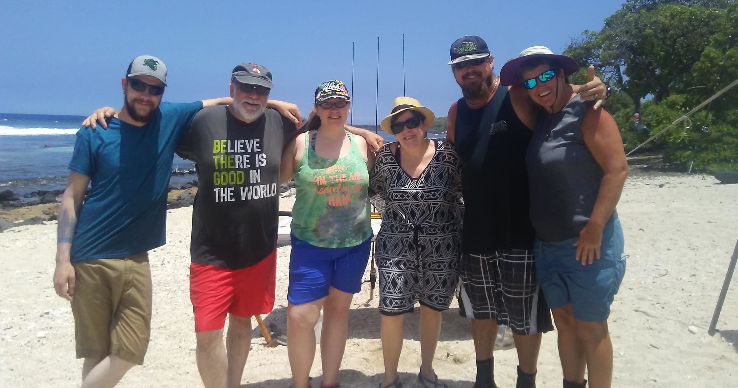 Group beach fishing party posing with rods on sandy shoreline