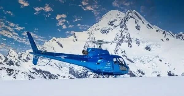 Blue helicopter parked on alpine snowfield near jagged peaks