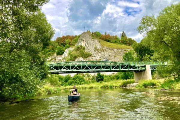 Solo kayaker paddling under green bridge on scenic forested river