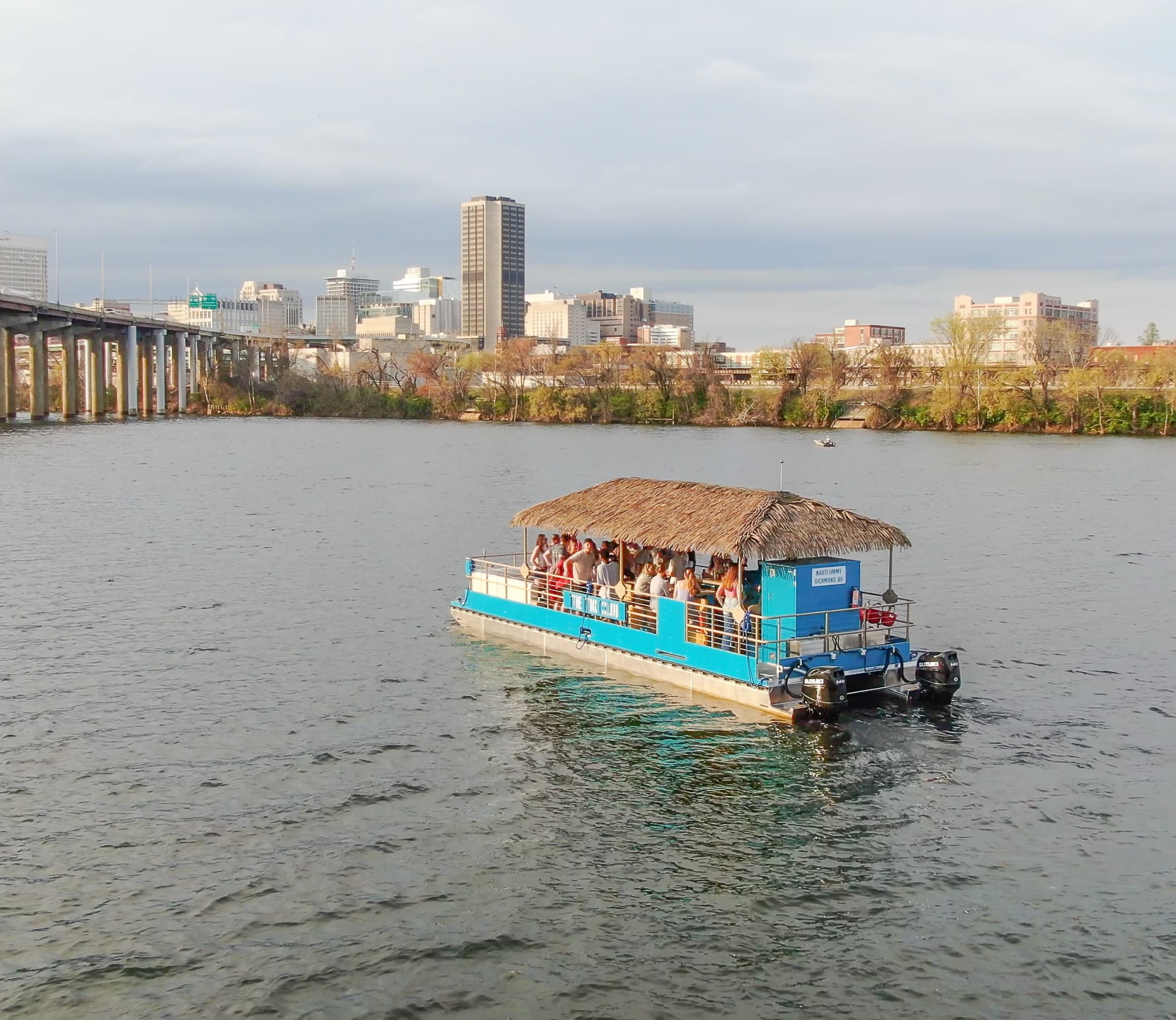Tiki-style party pontoon cruising river with city skyline