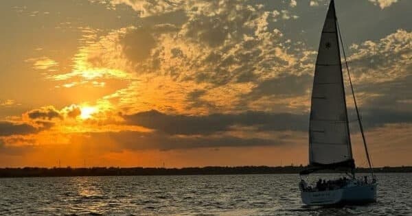 Sailboat silhouetted against golden sunset on bay