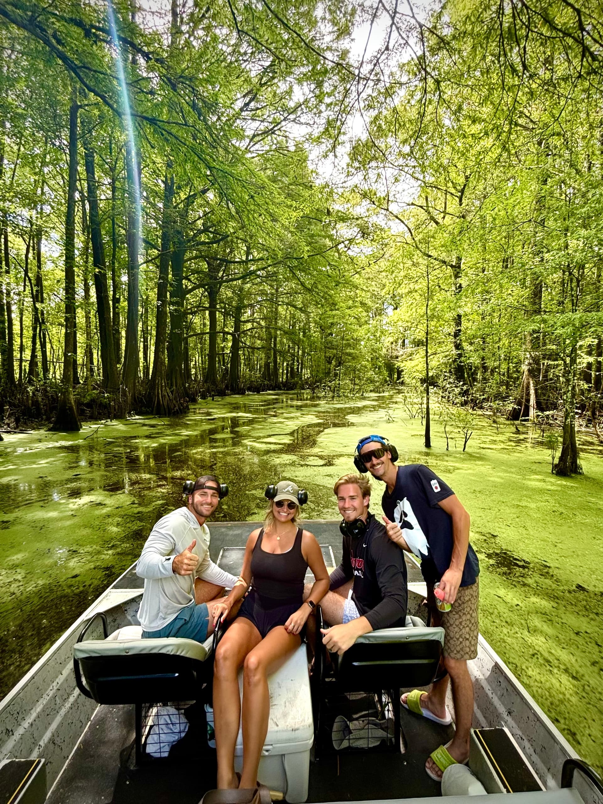 Four people on small boat cruising green cypress swamp waterway