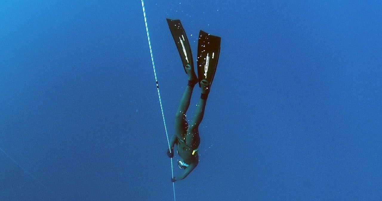 Freediver descending in deep blue open ocean, dramatic
