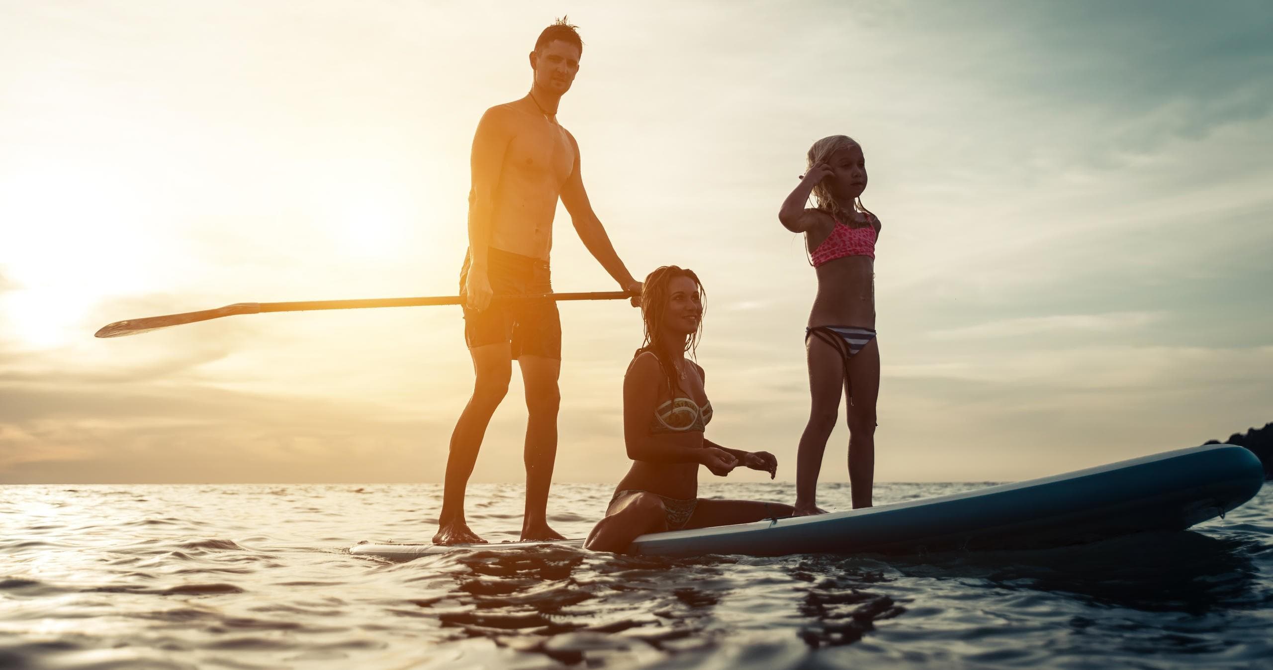 Family stand-up paddleboarding at sunset on calm ocean