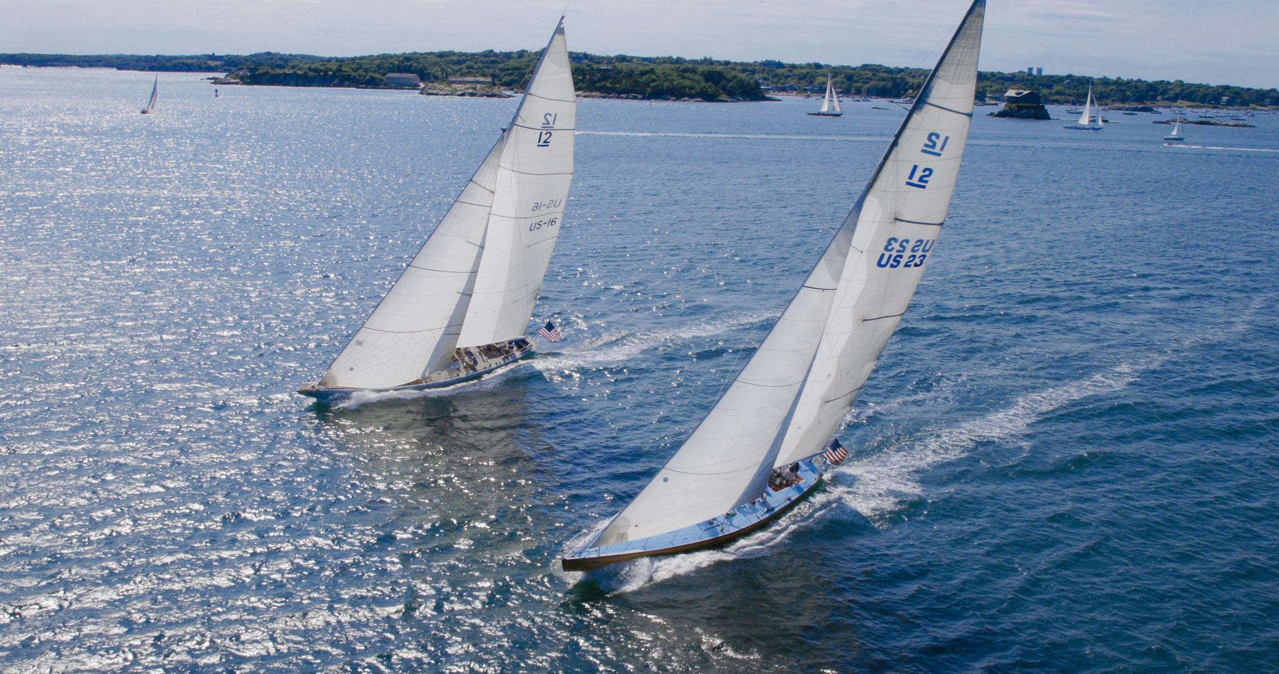 Two sailboats cutting through choppy blue harbor water, action shot