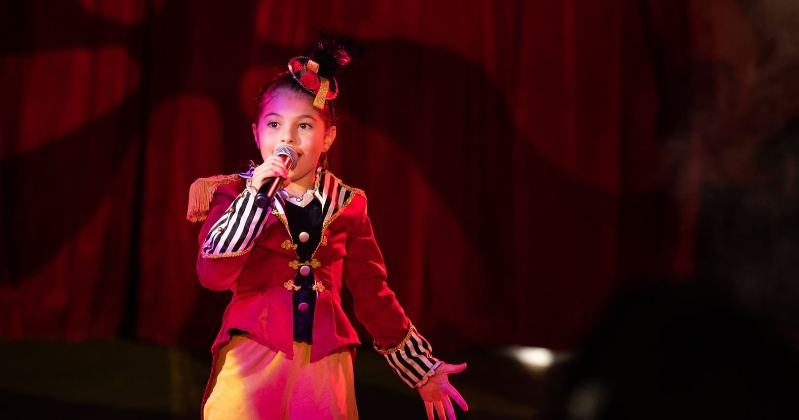 Young performer singing on circus stage under red tent lights