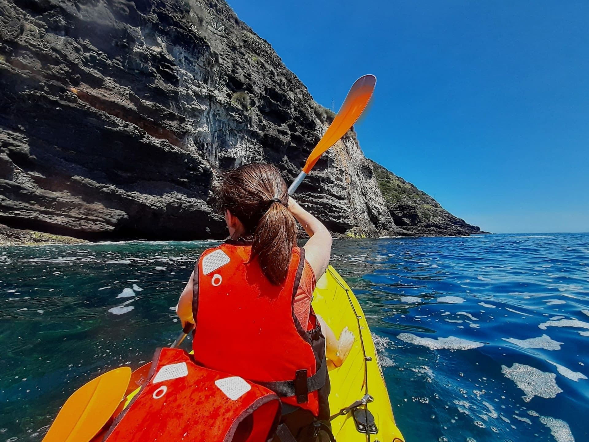 Kayaker paddling along Azores rocky coast, ocean adventure