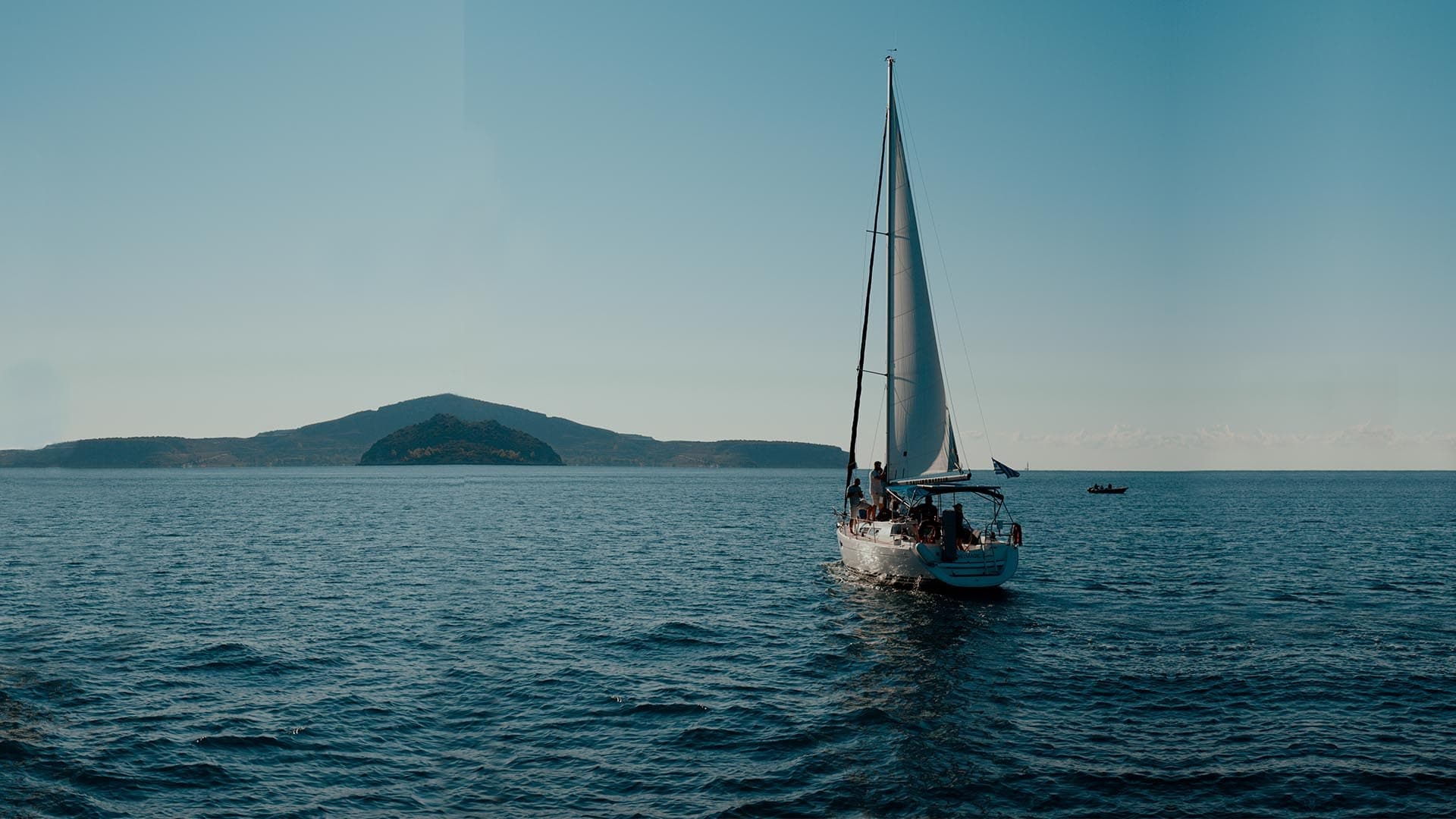 Sailboat cruising on open sea near island at sunset