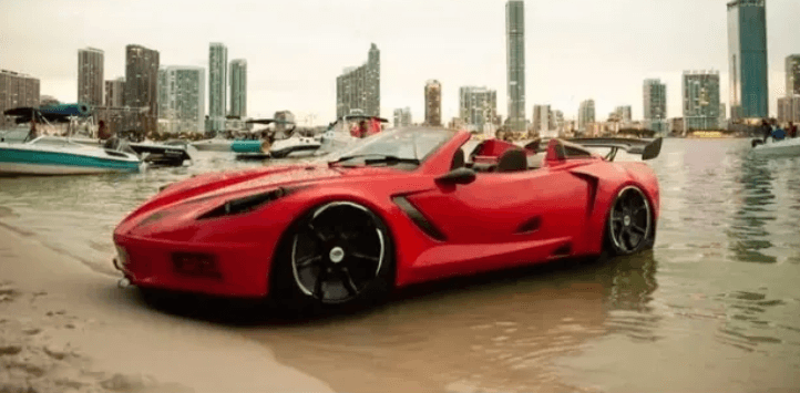 Red sports car parked on sandy beach with city skyline