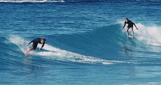 Pair of surfers carving blue waves off Oahu coast