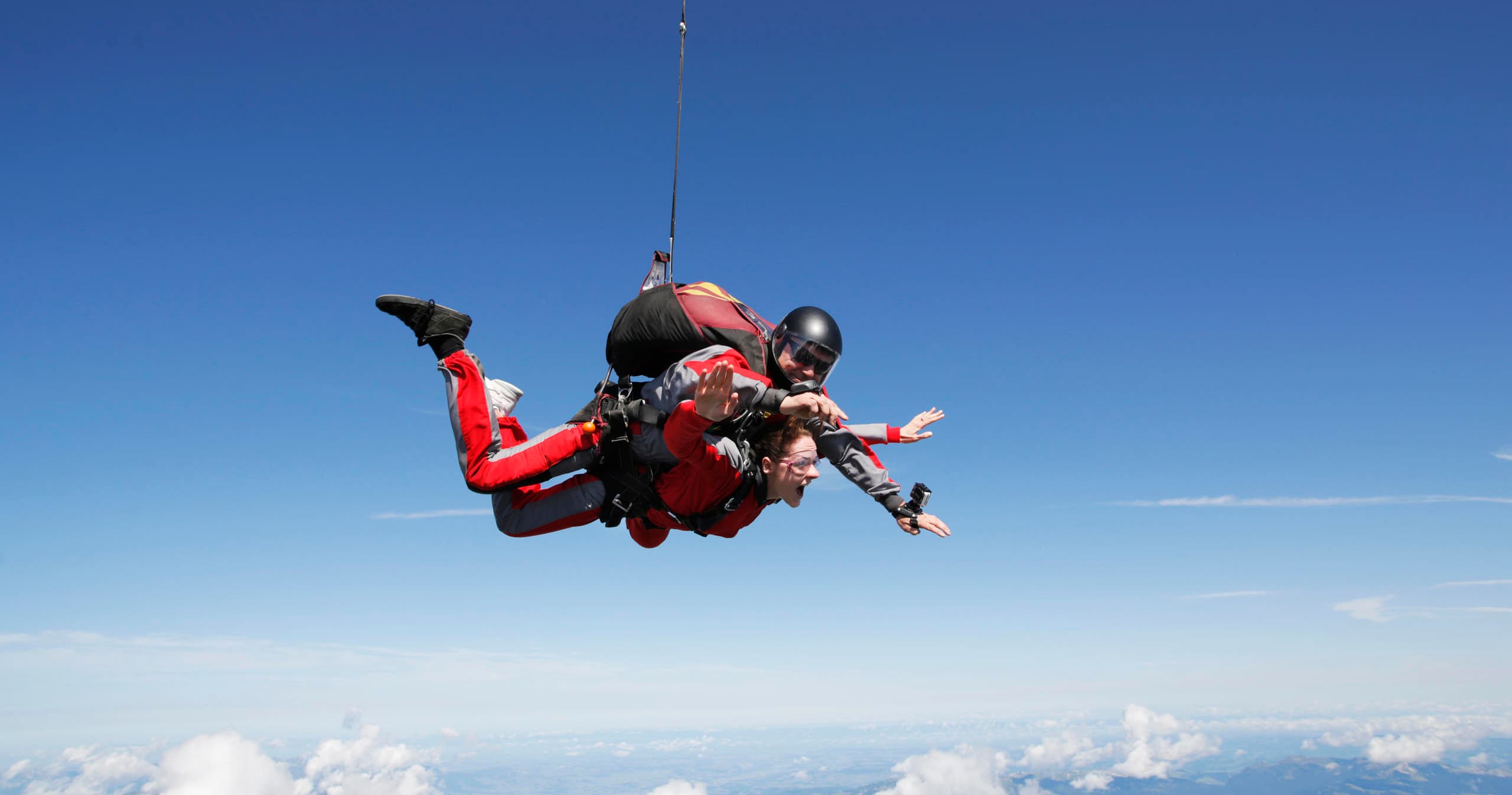 Tandem skydiver freefalling over clouds with alpine backdrop