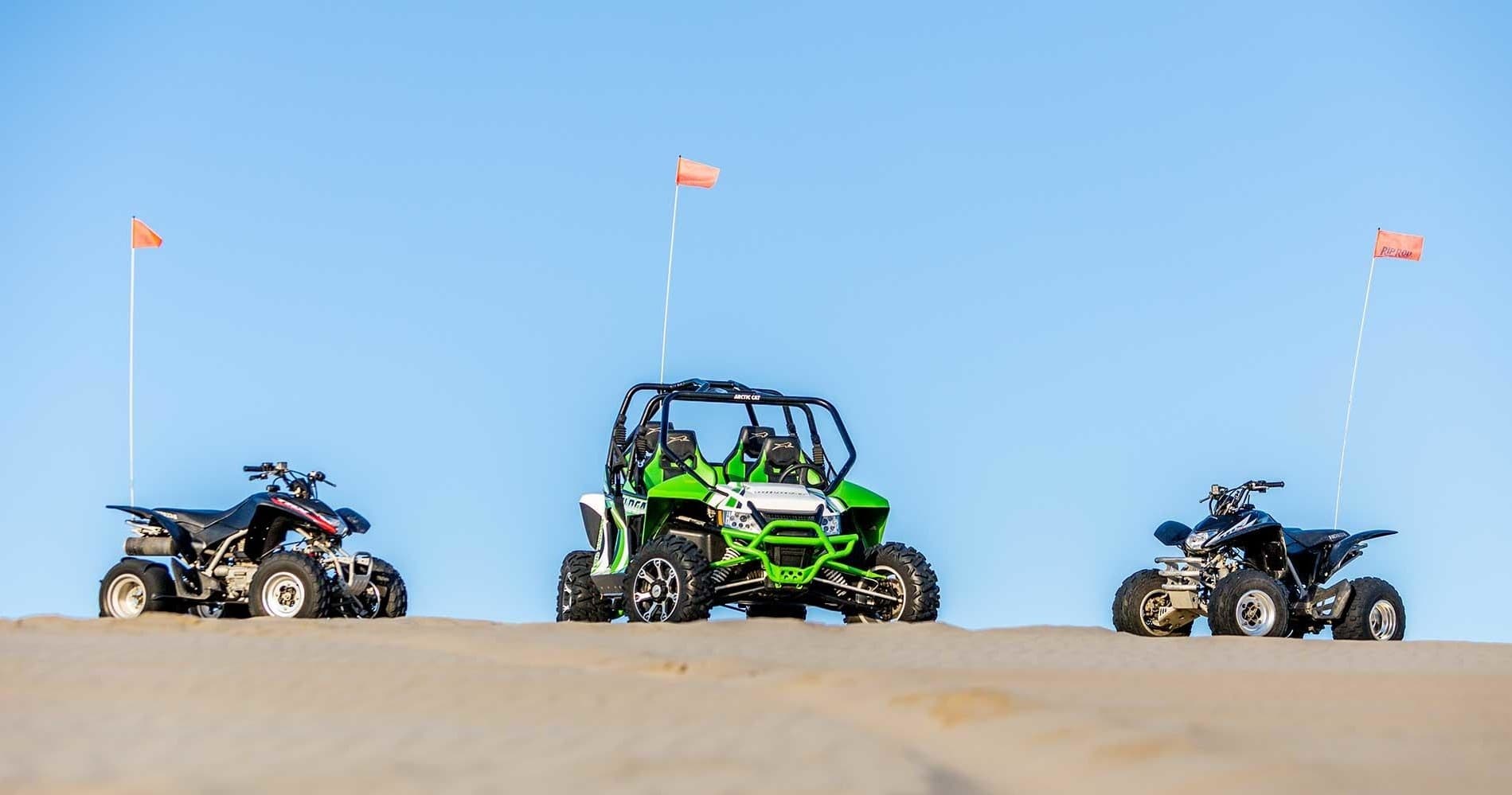Three ATVs lined on sand dunes under blue sky, dune riding
