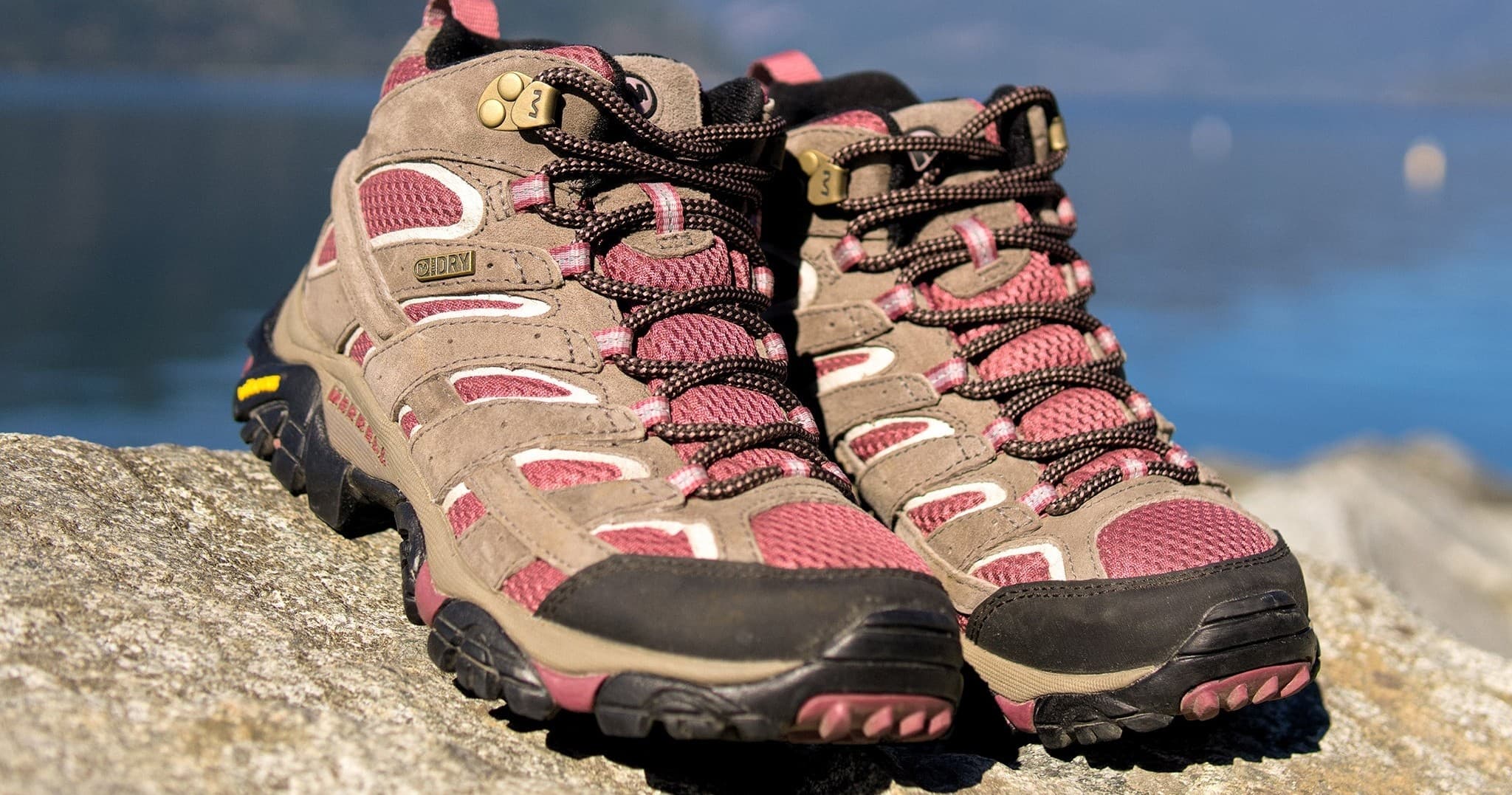 Trail hiking boots on rocky lakeshore, outdoor trekking gear
